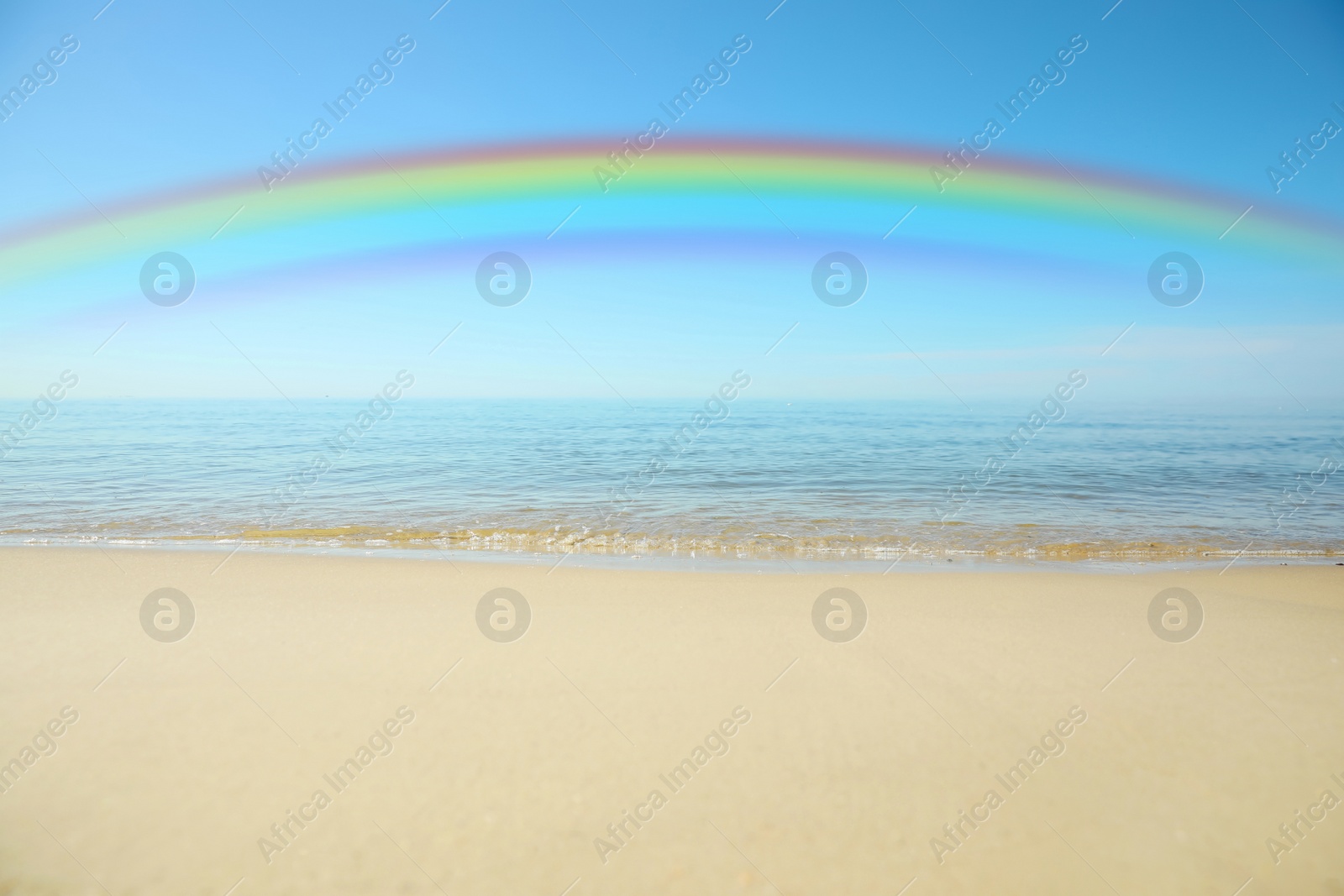 Image of Beautiful rainbow in blue sky over sandy beach and sea on sunny day