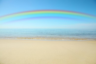 Beautiful rainbow in blue sky over sandy beach and sea on sunny day