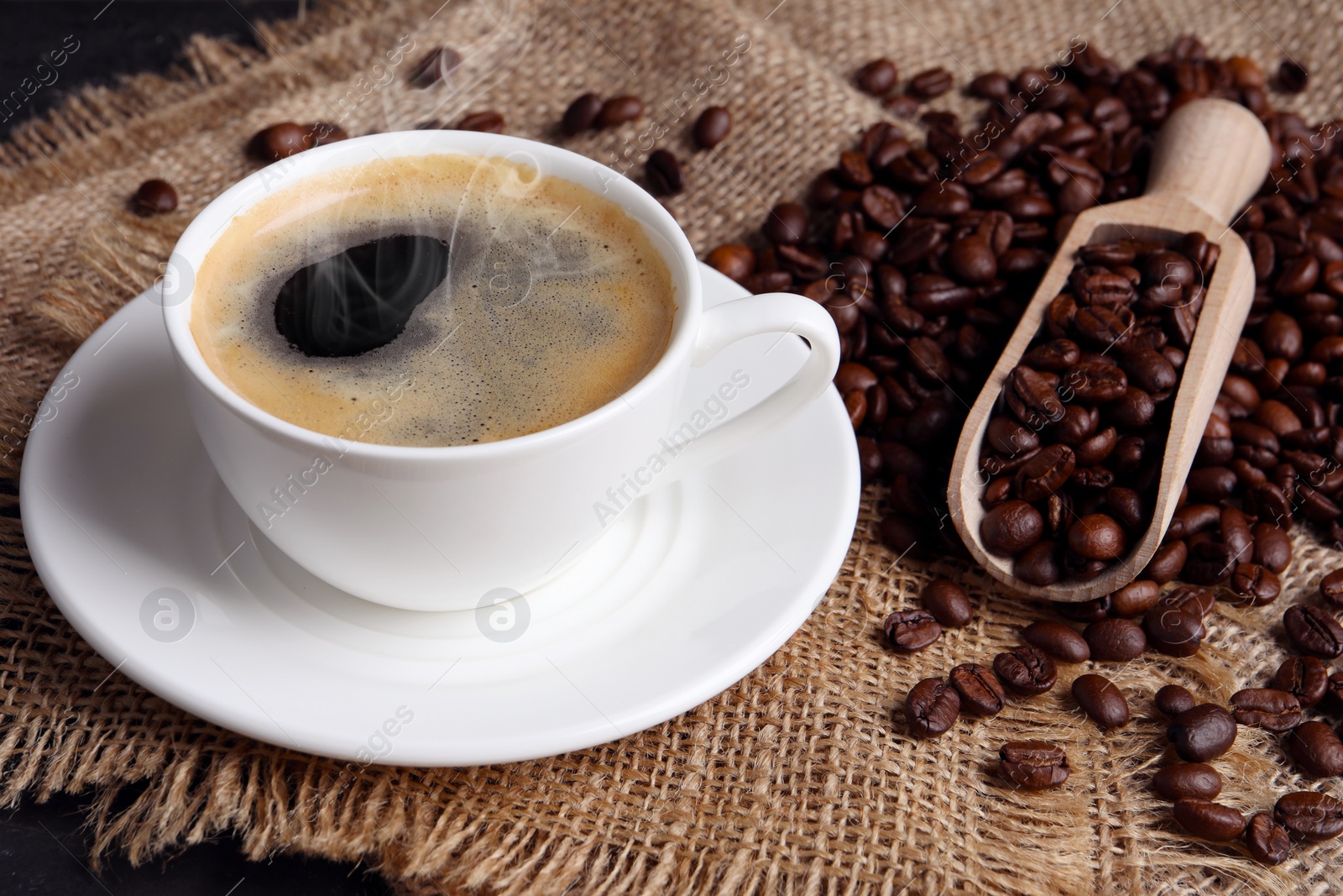 Image of Steaming coffee in cup and roasted beans on table