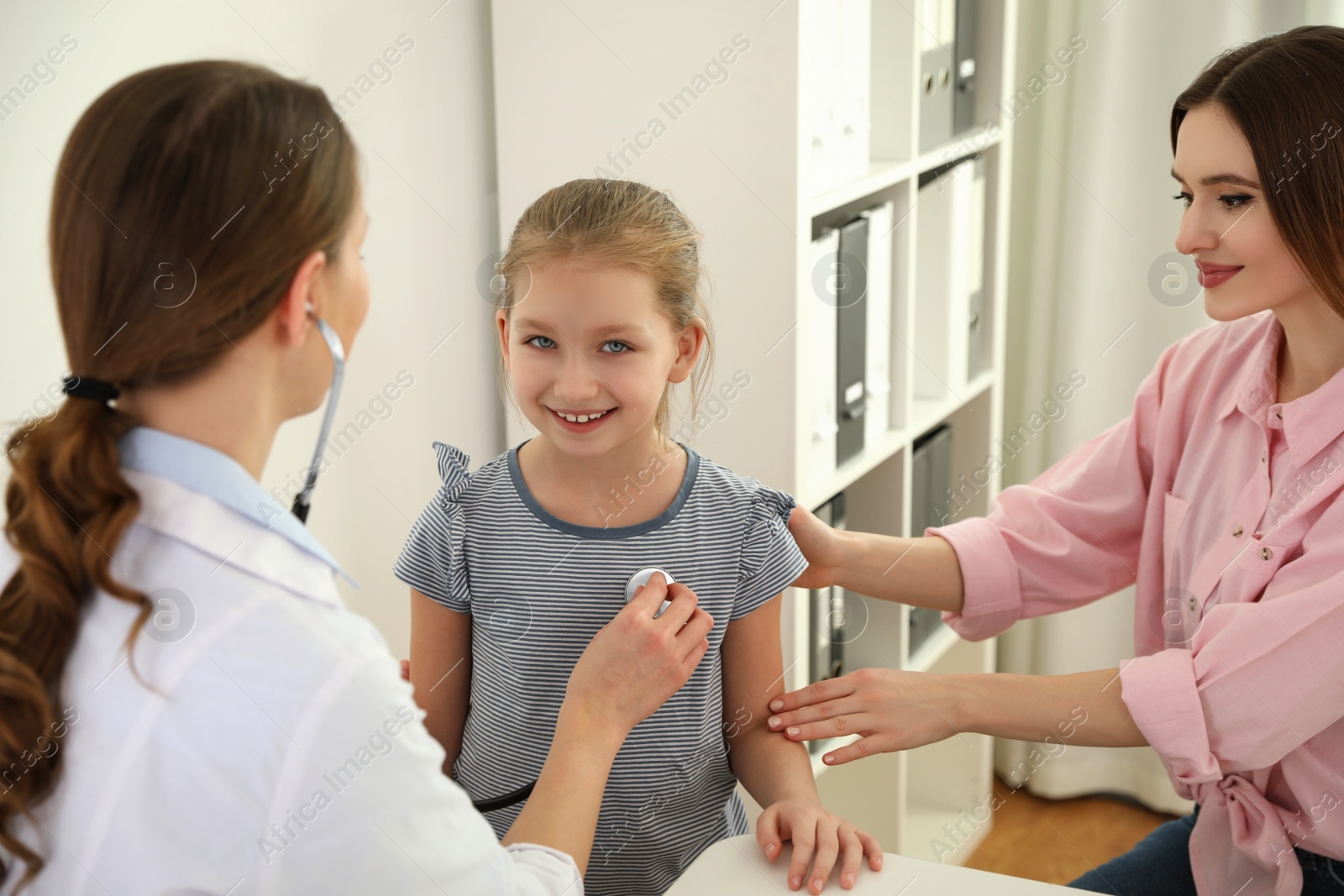 Photo of Mother and daughter visiting pediatrician. Doctor examining little patient with stethoscope in hospital