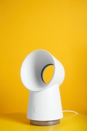 Photo of Modern electric fan on table against yellow background