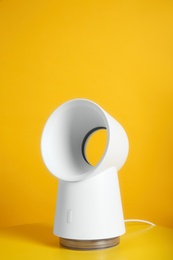 Modern electric fan on table against yellow background