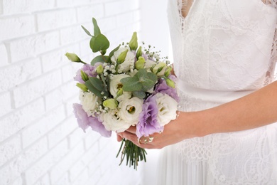 Photo of Bride holding beautiful bouquet with Eustoma flowers near brick wall, closeup
