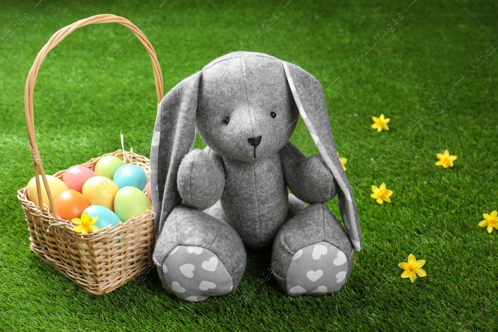 Photo of Cute Easter bunny toy and wicker basket with dyed eggs on green grass, space for text