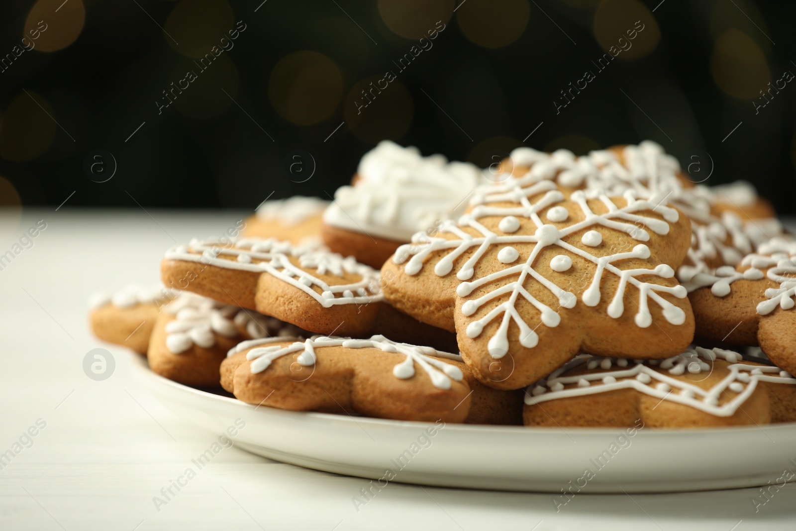 Photo of Tasty Christmas cookies with icing on white wooden table against blurred lights, closeup