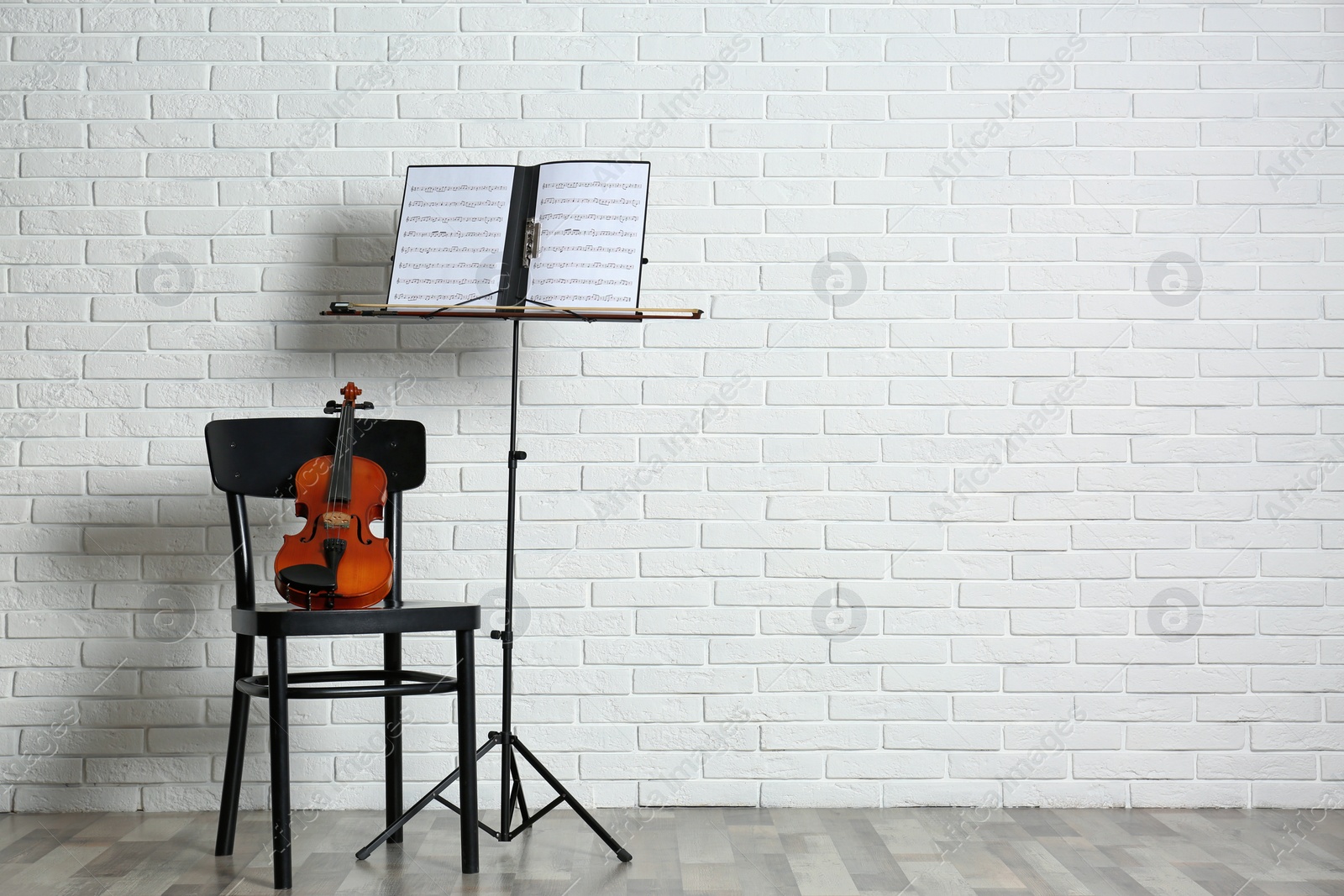 Photo of Violin, chair and note stand with music sheets near brick wall. Space for text