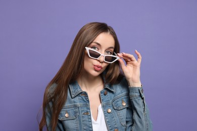 Photo of Beautiful young woman with sunglasses blowing kiss on purple background