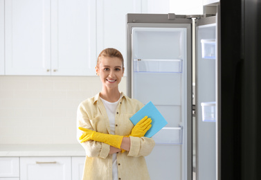 Young woman with rag near clean refrigerator in kitchen