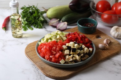 Photo of Cooking delicious ratatouille. Fresh ripe vegetables and plate on white marble table