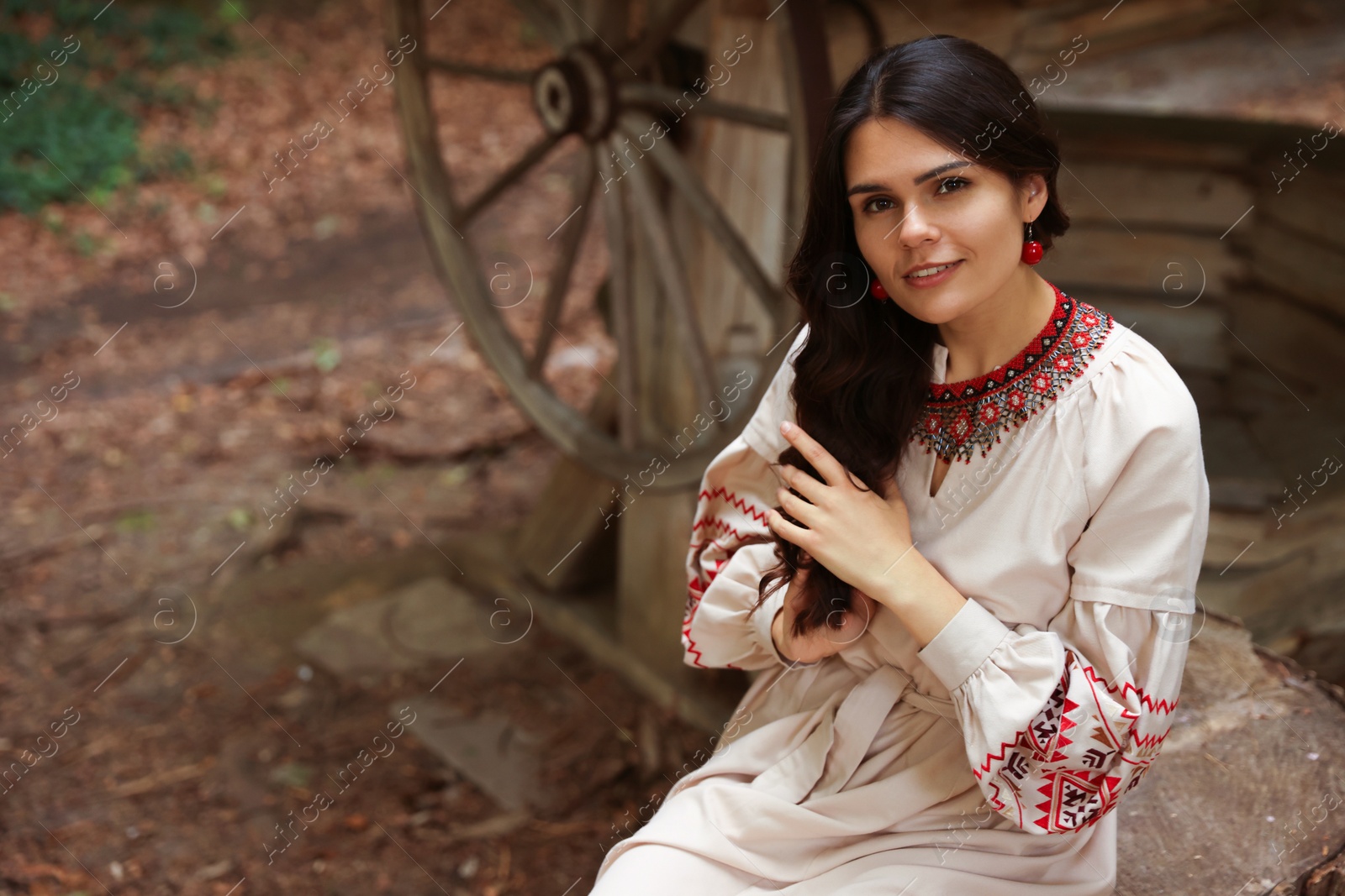 Photo of Beautiful woman wearing embroidered dress sitting near old wooden well in countryside. Ukrainian national clothes