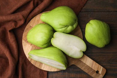 Cut and whole chayote on wooden table, flat lay