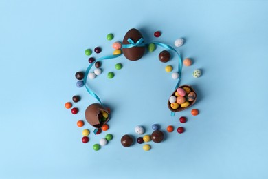 Photo of Frame made of tasty chocolate eggs and different candies on light blue background, flat lay with space for text