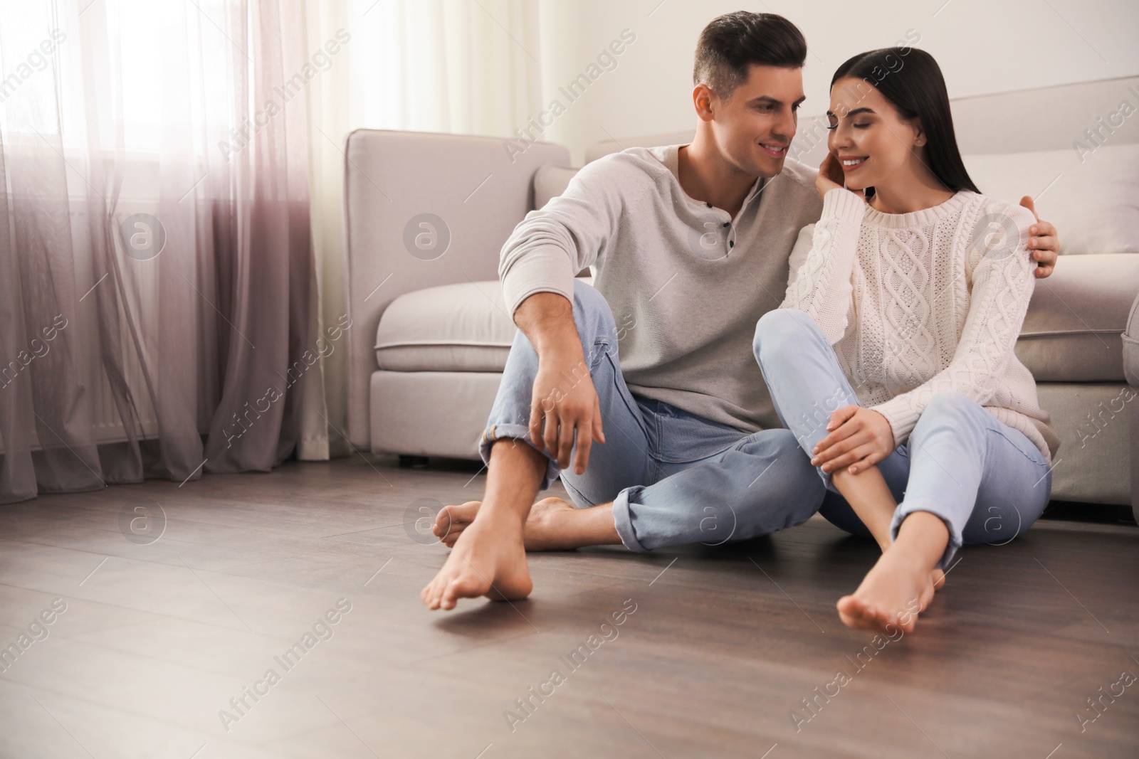 Photo of Happy couple sitting on warm floor in living room, space for text. Heating system