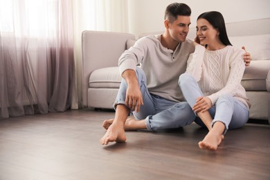 Photo of Happy couple sitting on warm floor in living room, space for text. Heating system