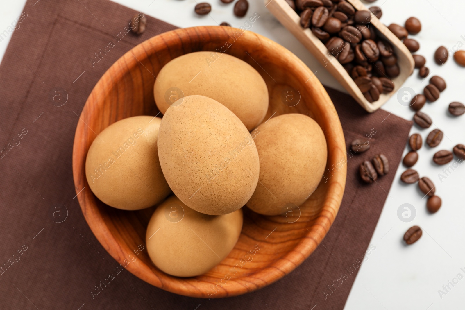 Photo of Easter eggs painted with natural dye in wooden bowl and coffee beans on white table, flat lay