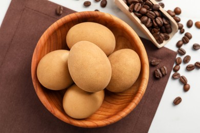 Easter eggs painted with natural dye in wooden bowl and coffee beans on white table, flat lay