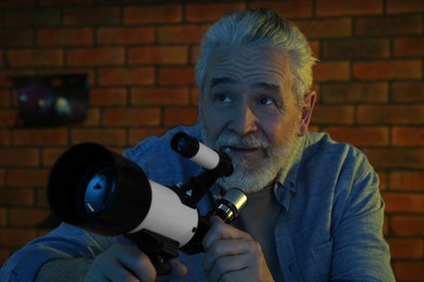 Photo of Senior man using telescope to look at stars in room