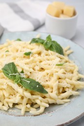 Plate of delicious trofie pasta with cheese and basil leaves on table, closeup