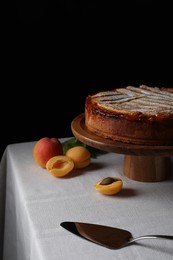 Tasty apricot pie with powdered sugar on table against black background