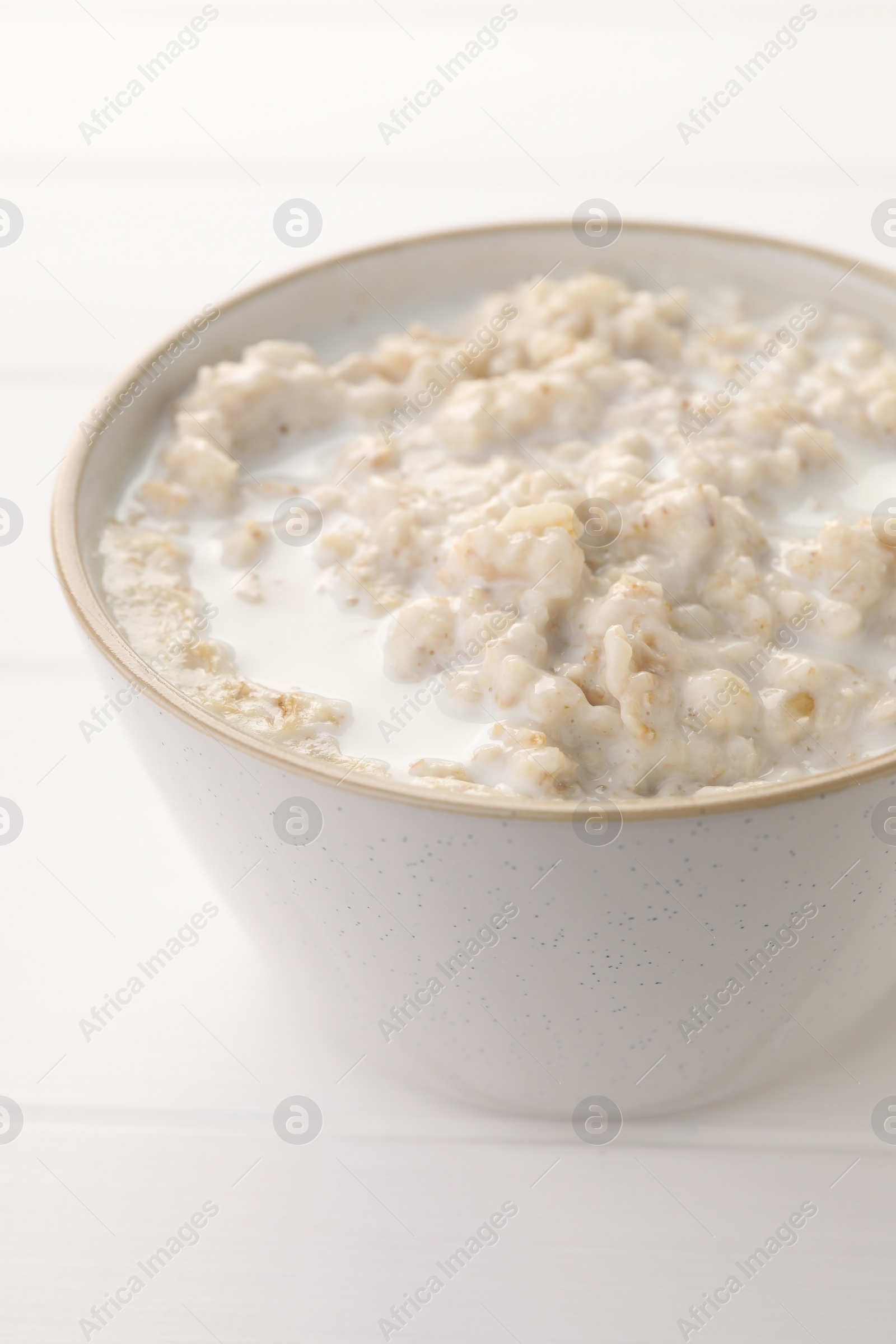 Photo of Tasty boiled oatmeal in bowl on white table, closeup