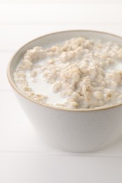 Photo of Tasty boiled oatmeal in bowl on white table, closeup