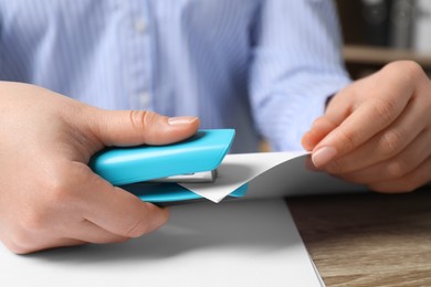 Photo of Woman stapling papers at wooden table indoors, closeup