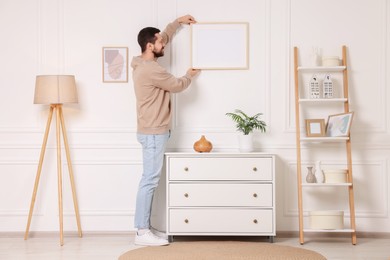 Man hanging picture frame on white wall at home