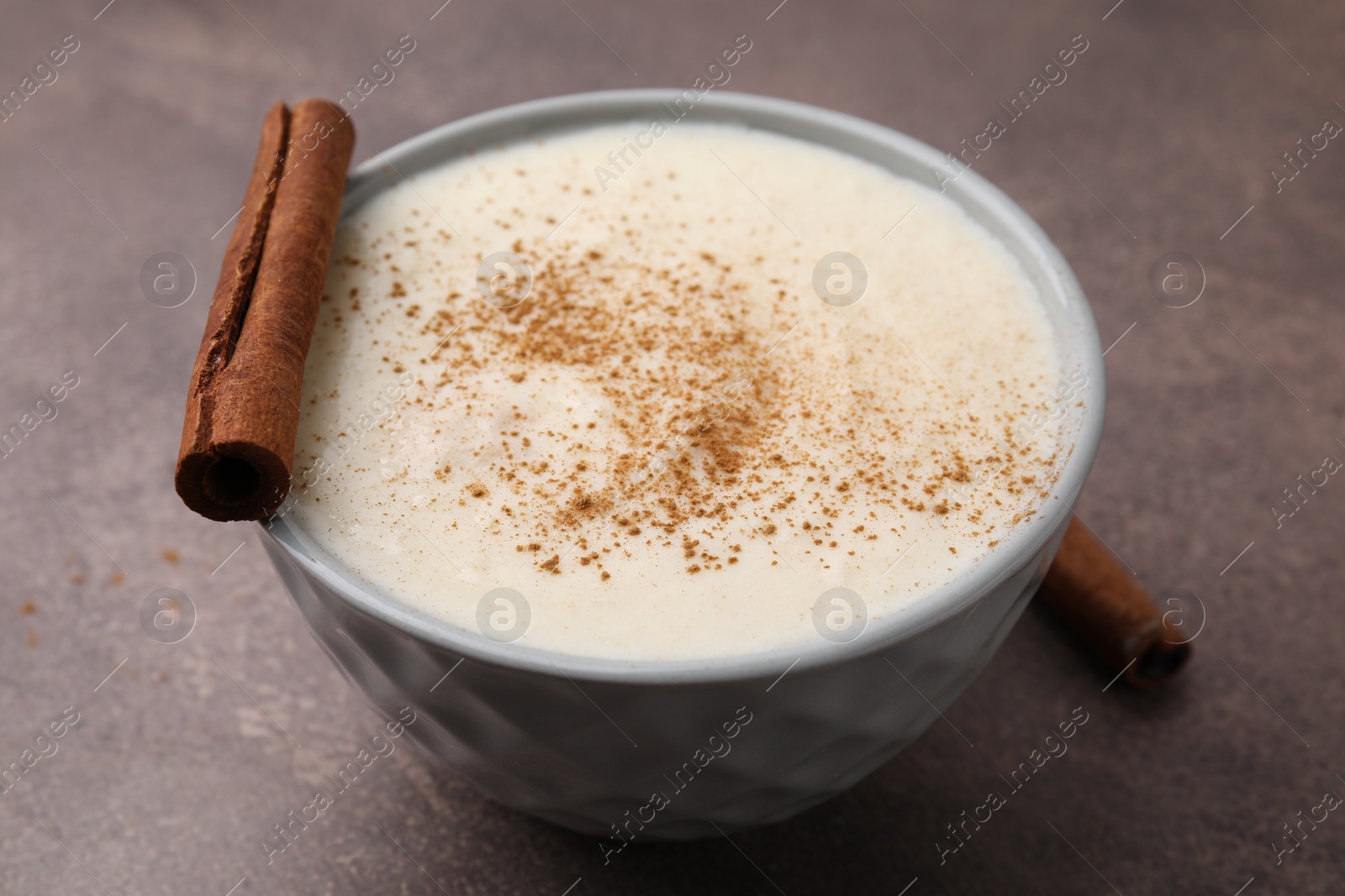 Photo of Delicious semolina pudding with cinnamon in bowl on brown table, closeup