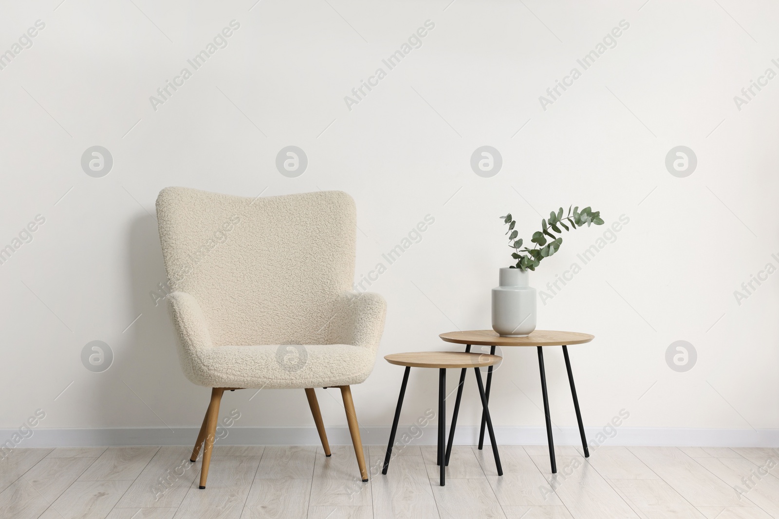 Photo of Comfortable armchair, nesting tables and eucalyptus indoors