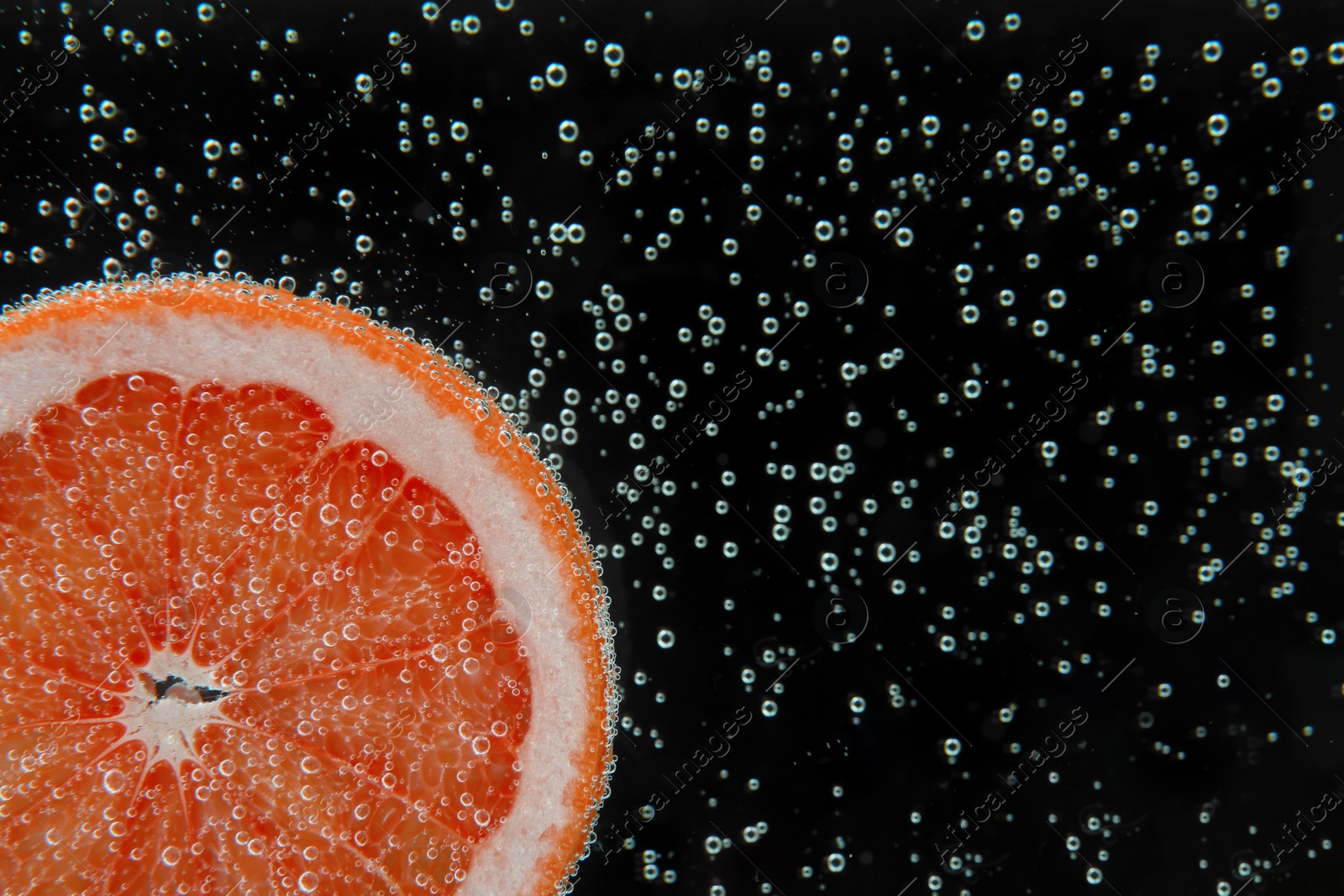 Photo of Slice of grapefruit in sparkling water on black background, closeup with space for text. Citrus soda