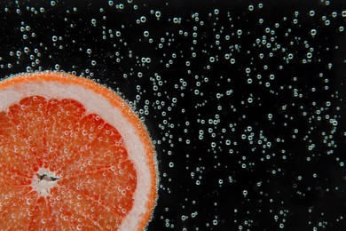 Photo of Slice of grapefruit in sparkling water on black background, closeup with space for text. Citrus soda