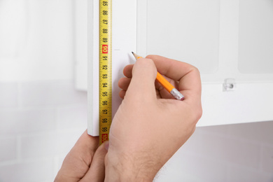 Photo of Worker measuring newly installed kitchen furniture, closeup