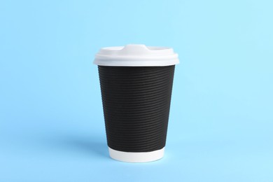 Black paper cup with plastic lid on light blue background. Coffee to go