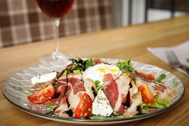 Photo of Delicious prosciutto salad with vegetables served on wooden table indoors