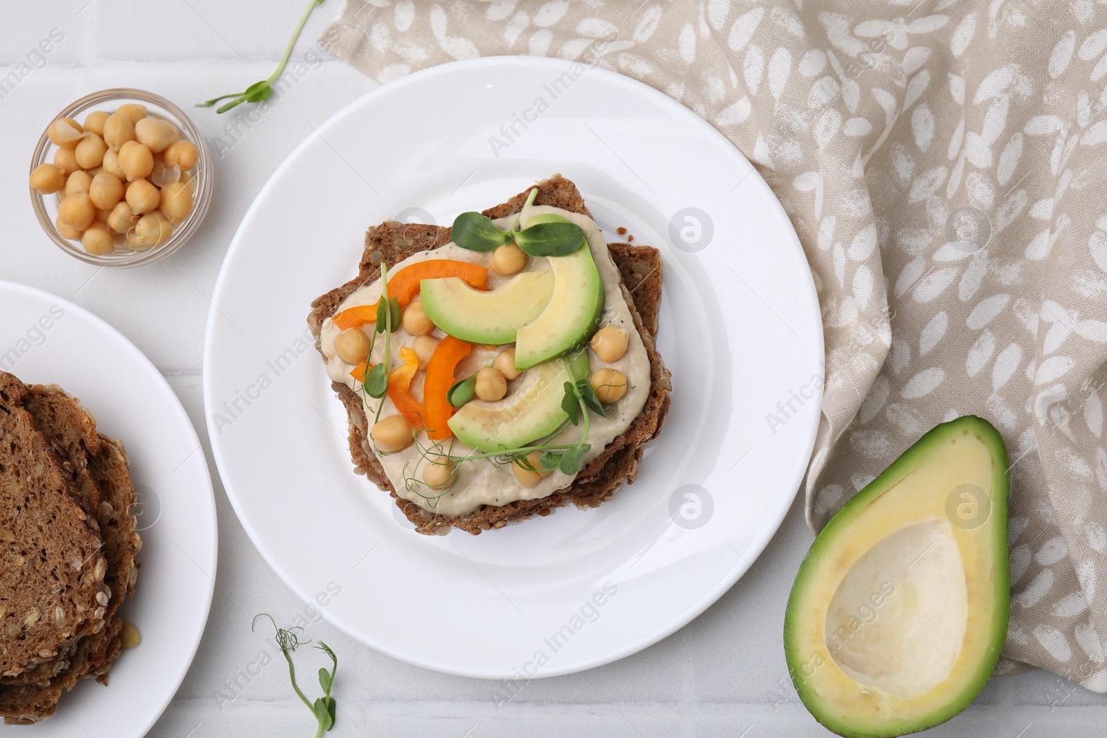 Photo of Tasty vegan sandwich with avocado, chickpeas and bell pepper on white tiled table, flat lay