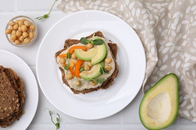 Photo of Tasty vegan sandwich with avocado, chickpeas and bell pepper on white tiled table, flat lay