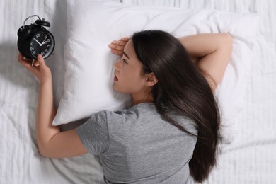 Woman looking at alarm clock on bed, top view. Insomnia problem