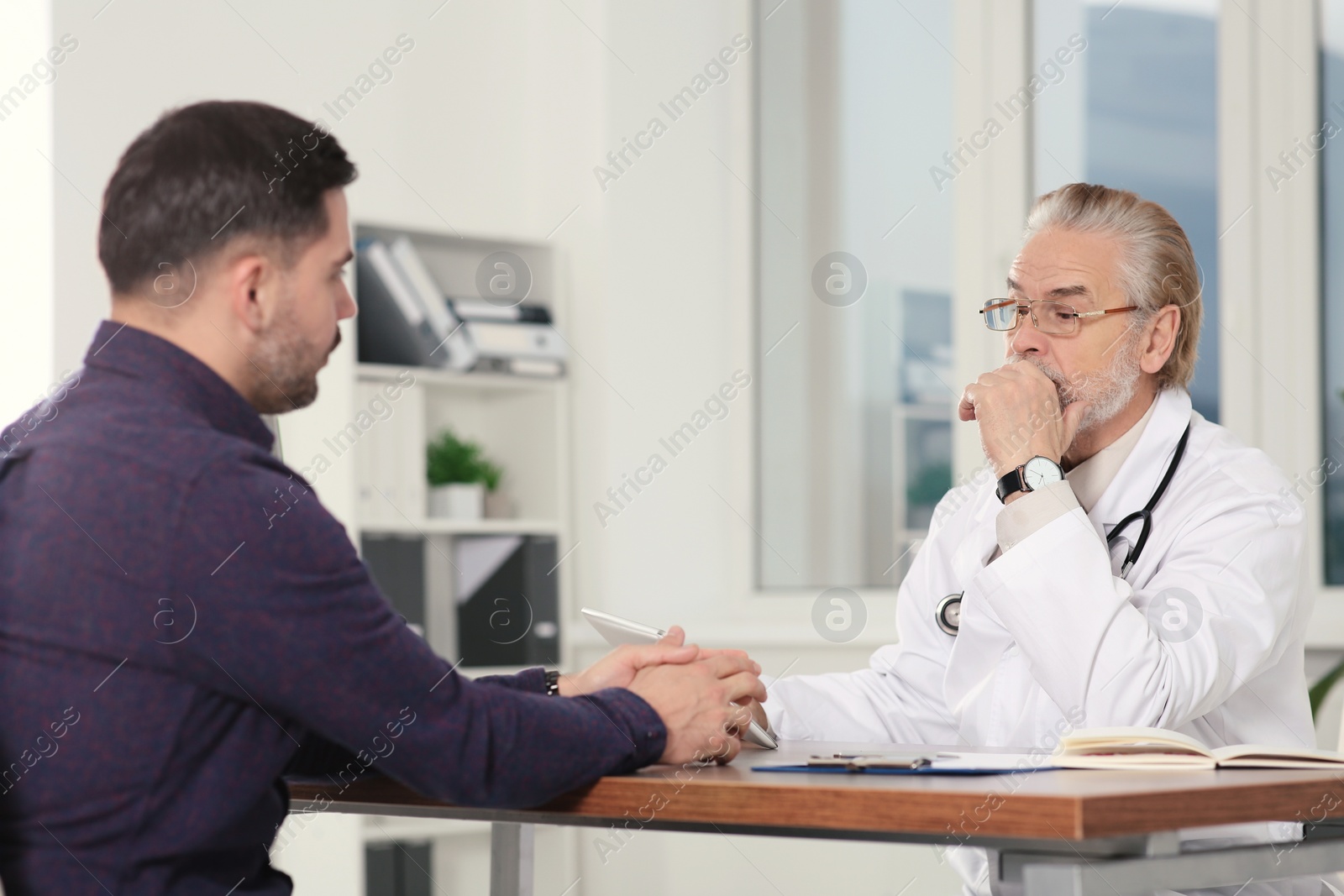 Photo of Senior doctor consulting patient at wooden table in clinic