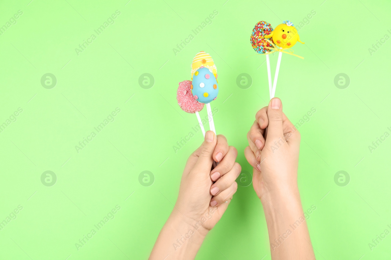 Photo of Closeup view of woman with delicious cake pops on light green background, space for text. Easter holiday