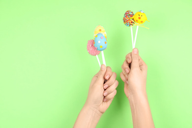 Closeup view of woman with delicious cake pops on light green background, space for text. Easter holiday