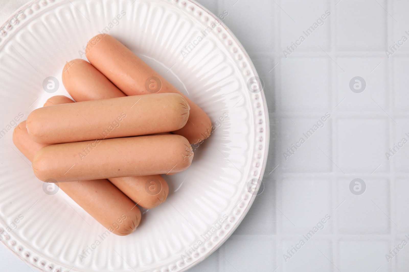 Photo of Delicious boiled sausages on white tiled table, top view. Space for text