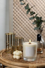 Photo of Burning soy candle, perfume and stylish accessories on wicker table indoors