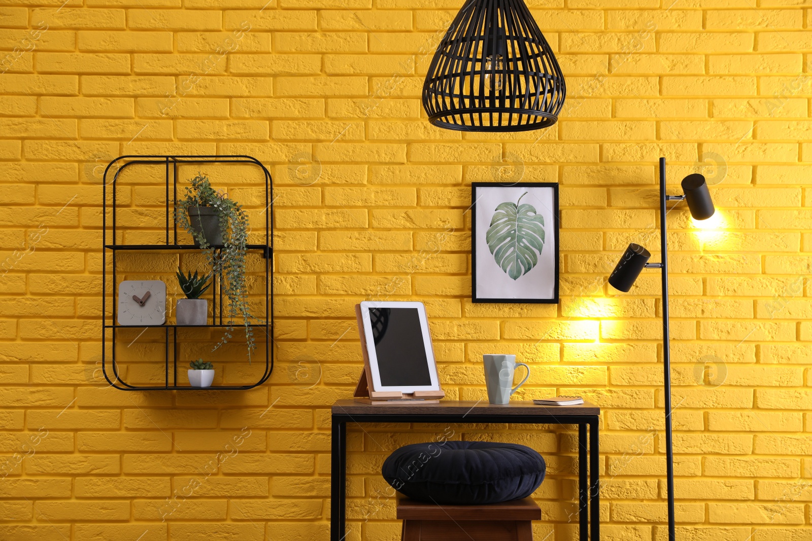 Photo of High wooden table with tablet and stool as stand up workplace near yellow brick wall. Stylish interior