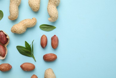 Fresh peanuts and leaves on light blue table, flat lay. Space for text