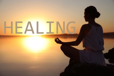 Woman meditating near river at sunset. Healing concept