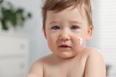 Photo of Cute little baby with moisturizing cream on face indoors