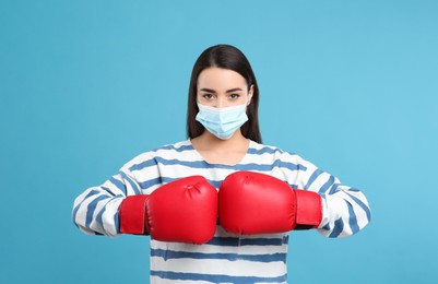 Photo of Woman with protective mask and boxing gloves on light blue background. Strong immunity concept