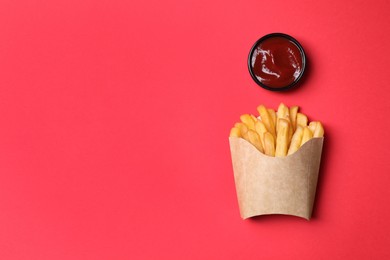Photo of Paper cup with French fries and ketchup on red table, flat lay. Space for text