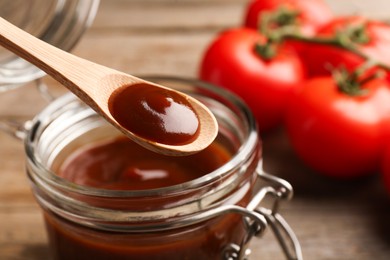 Photo of Taking tasty barbeque sauce from jar with spoon at table, closeup