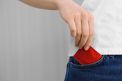 Woman pulling condom out of pocket indoors, closeup. Safe sex